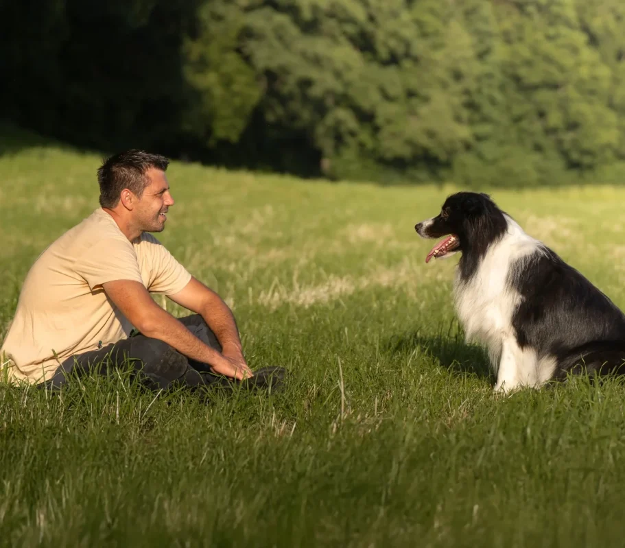 Hundetrainer Flo sitzt mit DreisamDog Hund Jaro auf einer grünen Wiese. 